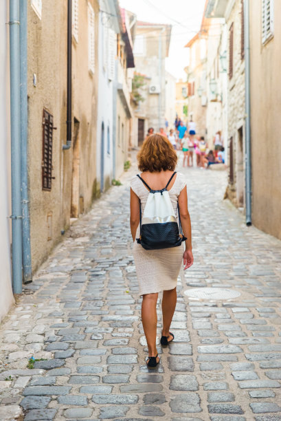一名年轻女子走在克罗地亚亚得里亚海小镇的街道上。克罗地亚Krk岛，一个女孩走在Krk老城的街道上。旅游和假日概念。图片下载