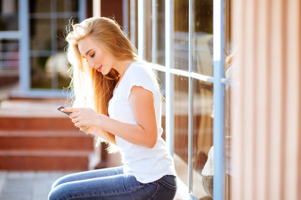 迷人的微笑女人在户外使用智能手机。图片下载