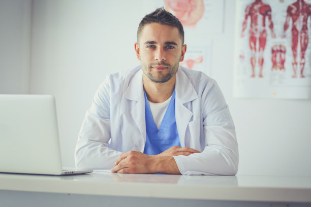 一名男性医生的肖像与笔记本电脑坐在办公桌上的医疗办公室图片下载