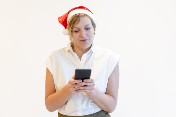 沉思的中年商务女士戴着圣诞帽使用智能手机图片下载