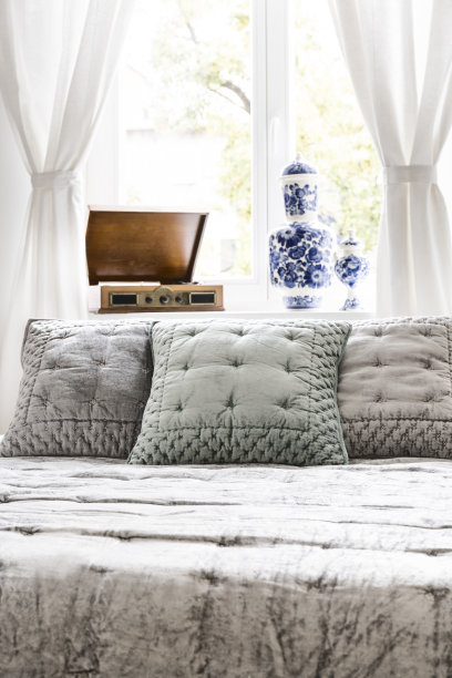 银色天鹅绒床罩和枕头的特写，在一个明亮的窗户背景在一个阳光充足的卧室内部。真实的照片。图片下载