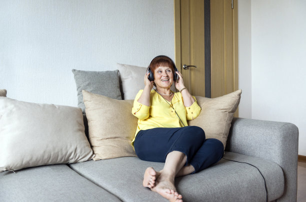 成年白人女子戴着耳机在房间的沙发上听音乐并大笑，穿黄色衬衫的女子，笑着的女子图片下载