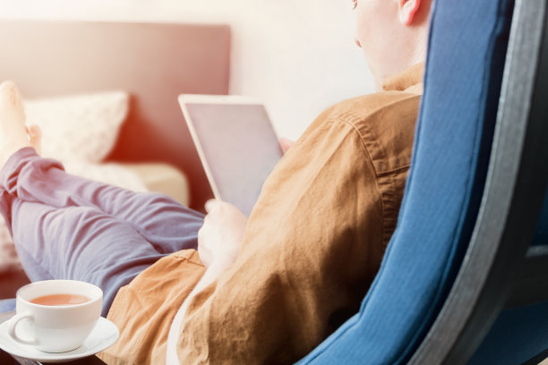 这张照片摄于男人的肩上，此时他正忙着平板电脑的规划工作和在家的休闲时光。商业和自由职业的概念。有选择性的重点。图片下载