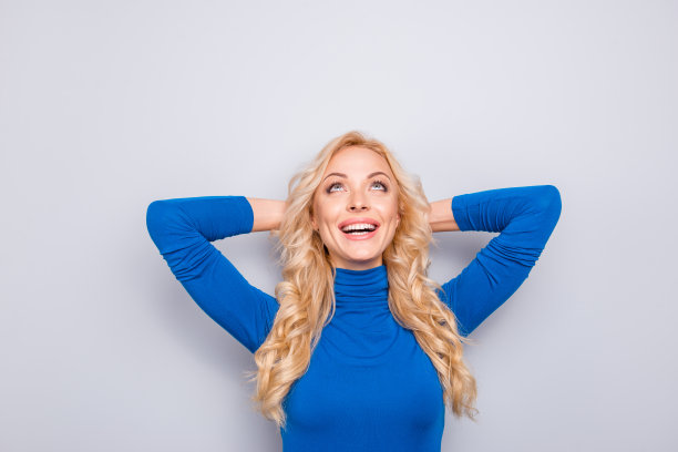 漂亮的，时髦的，迷人的，可爱的，笑的，兴奋的，快乐的女人在蓝色高领手背在脑后，向上看，孤立在灰色的背景图片下载