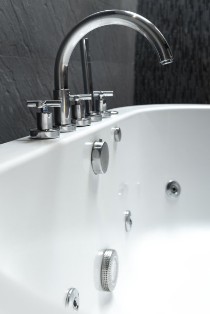 现代水龙头和白色的石头浴缸和深灰色的石头瓷砖墙壁在现代豪华浴室内部图片下载