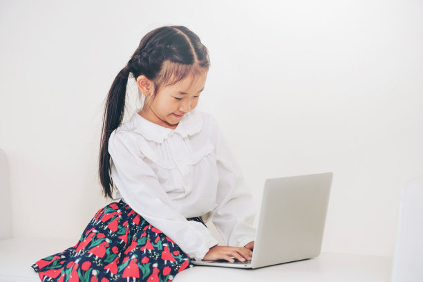 一个小孩在白色的沙发上使用笔记本电脑。图片下载