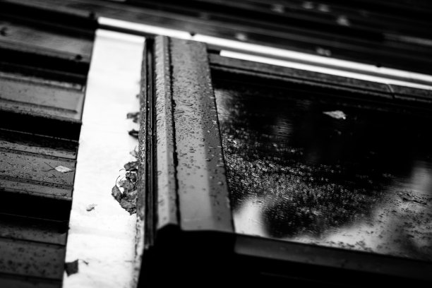 在这张高对比度的黑白图像中，一个金属窗框被雨滴覆盖。图片下载