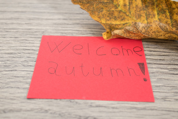 在一张木桌上的红纸上，手写着欢迎秋天的字样图片下载