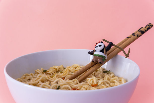 功夫熊猫玩具从动画喜剧武术筷子滑动，在面条碗与淡粉色的背景图片下载