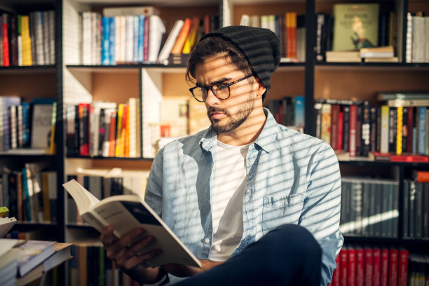 可爱的时尚男孩坐在图书馆地板上好奇地翻阅书籍。图片下载