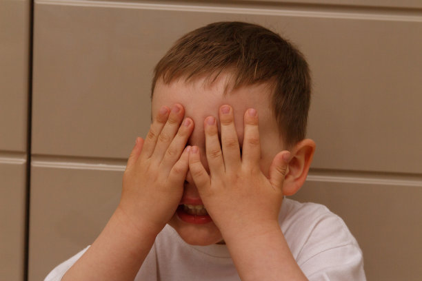 穿白色t恤的男孩用手闭上了眼睛。隐藏、哭泣,害怕。图片下载