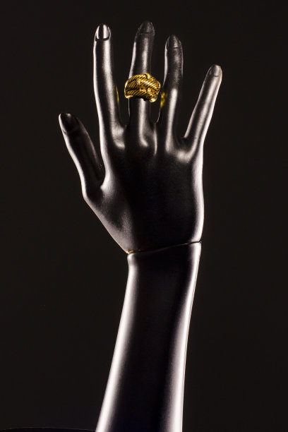黑色的塑料假人的手，黑色背景，手指上戴着金戒指图片下载