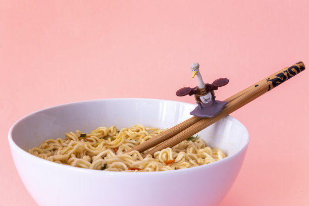 阿宝先生把动画片《功夫熊猫》的养父玩具和筷子放在一个粉粉背景的面条碗里图片下载