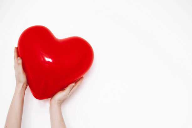 手中拿着的心。情人节快乐。红色的心形气球在白色的背景和文字空间。保健、医药、献血理念。爱和保护图片下载