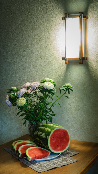 靠墙的木桌上放着一个玻璃花瓶，里面放着成熟的带花的条纹西瓜片，在一盏壁灯的柔和的半黑暗中图片下载