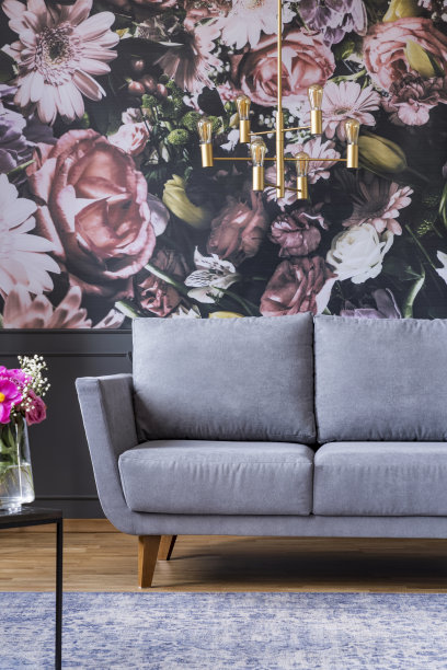 客厅室内灰色长沙发上方的金色枝形吊灯，墙上印有花朵图案。真实的照片图片下载
