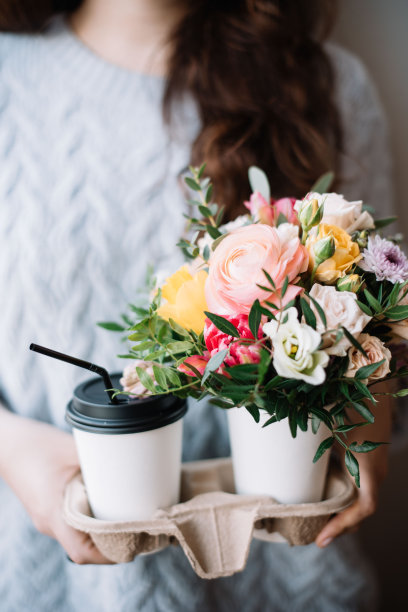 非常漂亮的年轻女子拿着两个外带咖啡杯与卡布奇诺在一个和小花束在另一个，近距离观看图片下载