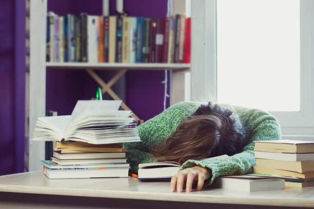 一个穿着绿色毛衣的女人睡在一堆书和学习材料中间的桌子上图片下载