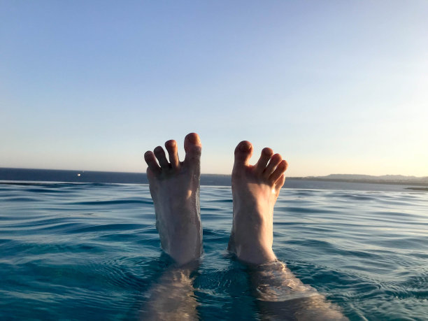 男腿，脚与手指摊开在一个美丽的蓝色潮湿的天蓝色自然清澈的水对着蓝色的天空和地平线在一个热带温暖的海边度假胜地图片下载