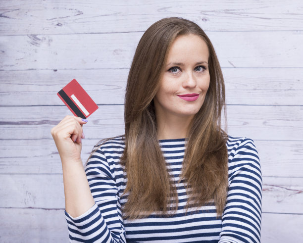女孩与长头发在背心拿着一张银行卡在她的手，1年轻的白人妇女与信用卡图片下载