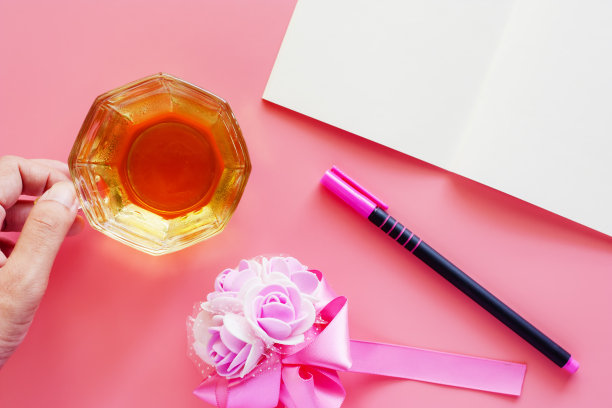 一杯咖啡与打开的笔记本，钢笔和鲜花在粉红色的背景放松的工作概念图片下载