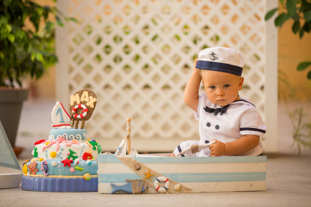 一个蹒跚学步的小男孩，打扮成水手，用海洋主题蛋糕、船、鱼和水生动物庆祝他的第一个生日图片下载