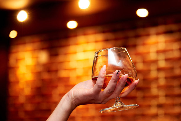 在模糊的背景上，女孩的手握着一杯白兰地图片下载