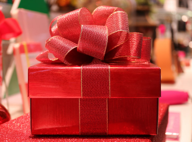 在模糊的背景上有闪光的红色丝带蝴蝶结的红色方块礼盒的正面视图图片下载