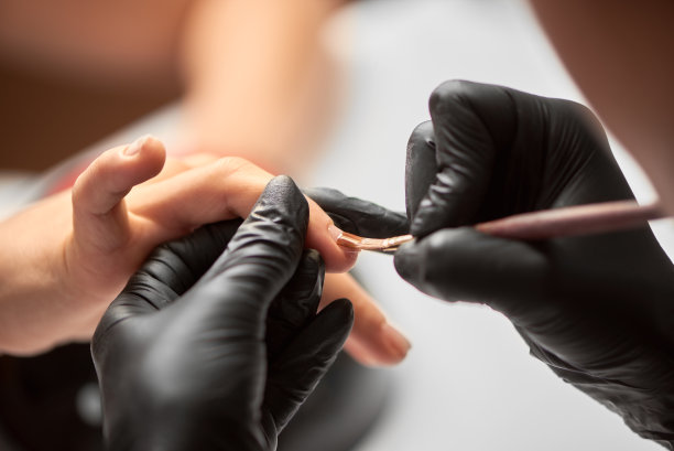 特写的美容师的手应用透明的指甲油在美容沙龙的女人指甲。图片下载