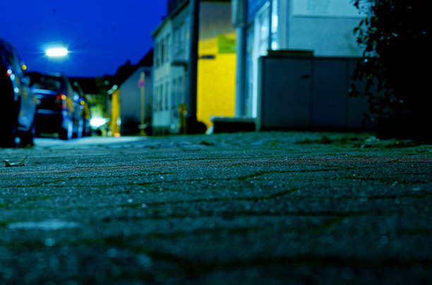 在一个城市的人行道上，以狭窄的鹅卵石为焦点，而市中心在背景中失去焦点，浅聚焦渐变和蓝色，冷色配黄色。图片下载