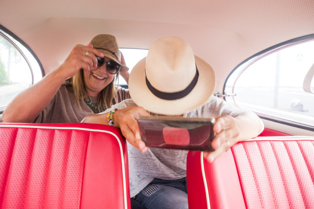 一对女性白人朋友享受一辆红色古董车与现代智能手机自拍。对比新事物相关的技术。乐趣和享受的概念图片下载