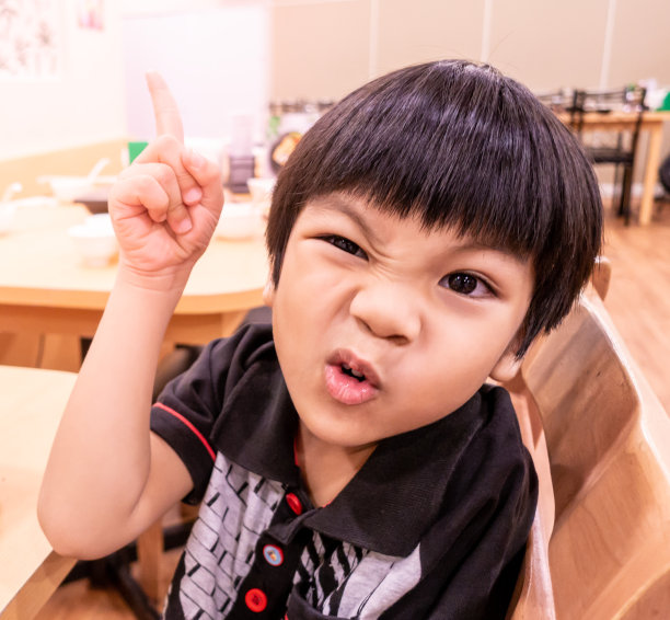 饥饿有趣的孩子摆出生气的姿势在餐厅等待食物。图片下载