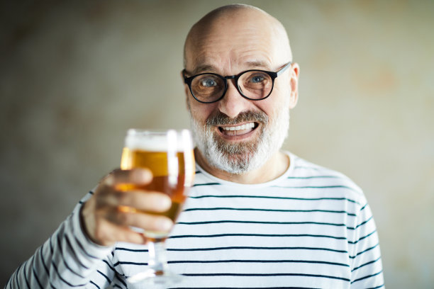 肖像欣喜若狂的困惑英俊的成熟男子皱着眉头喝啤酒和说祝酒词，同时举起啤酒杯图片下载