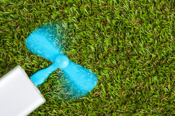 一个蓝色的usb风扇插入蓝色的动力库，并在绿色草地的背景下旋转，有拷贝空间图片下载