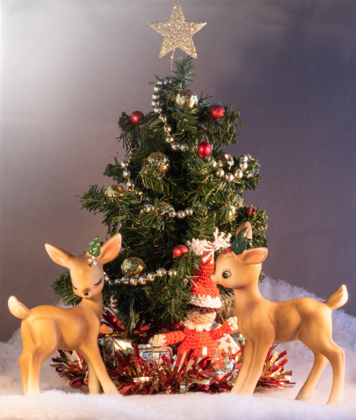 两尊迷人的复古小驯鹿雕像，放在装饰着礼物的迷你圣诞树前图片下载