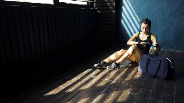 适合的年轻女子运动包坐在地板上，用绷带包扎手图片下载