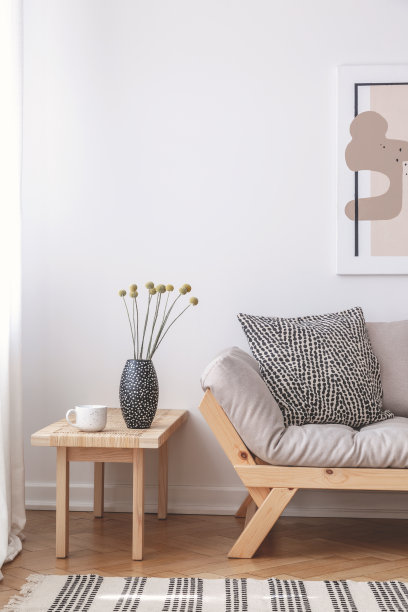 木桌上放着鲜花，旁边是米色沙发，沙发上有靠垫，室内平整，配有海报。真实的照片图片下载