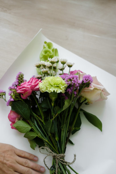 粉红色的康乃馨和玫瑰花束。女花匠在室内制作花束。女花匠在花店准备花束图片下载