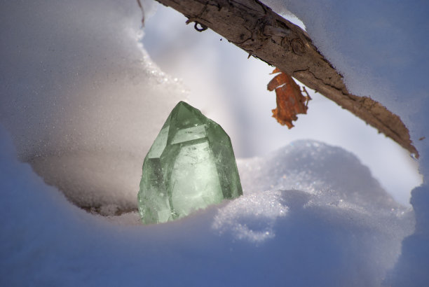 大的发光水晶透明的绿色石英在阳光下对雪冬天的背景特写图片下载