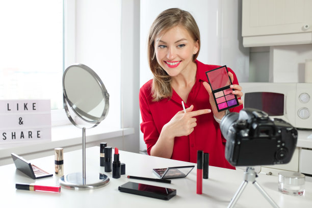 水平的特写，年轻的欧洲俄罗斯妇女已经把化妆品放在厨房的桌子上，拿着明亮的嘴唇调色板，指着最好的颜色显示给她的美丽博客的订阅者，微笑着图片下载