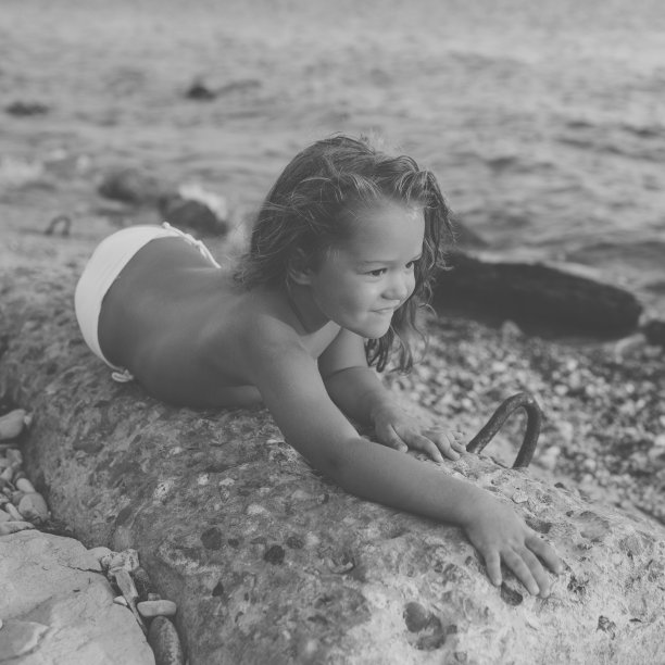 小女孩躺在海边的一块石头上，微笑着。黑白图像图片下载