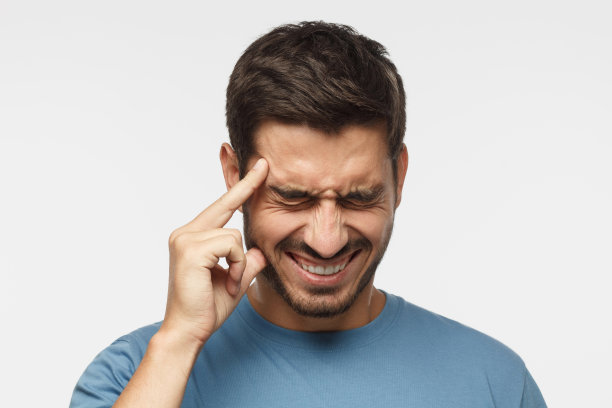 头痛的概念。一个年轻人被孤立在灰色的背景中，显示出他的头有多疼，经历着痛苦，看起来痛苦而疲惫图片下载