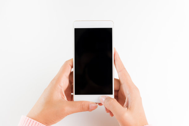 白色桌子背景上的女人手持白色手机智能手机。图片下载