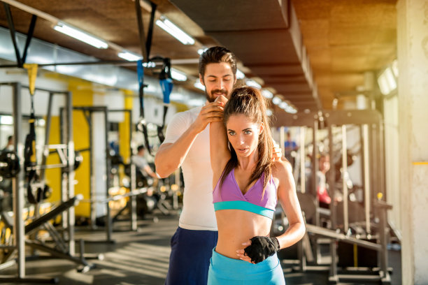 强壮的私人健身教练帮助他的女性客户伸展手臂的图片。在健身房训练。图片下载