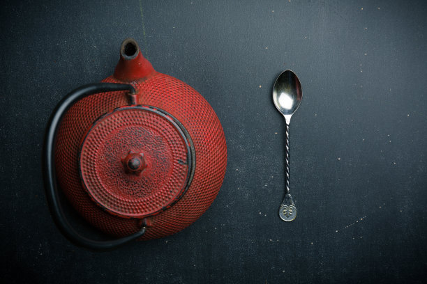 黑色背景上的红色茶壶和银色汤匙图片下载
