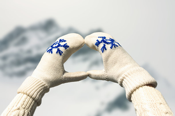 在冬天，女性的手在一个心形的连指手套对面的雪山和阿尔卑斯湖在冰天雪地图片下载