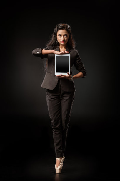 迷人的女商人穿着西装和芭蕾舞鞋，在黑色背景下展示平板电脑图片下载