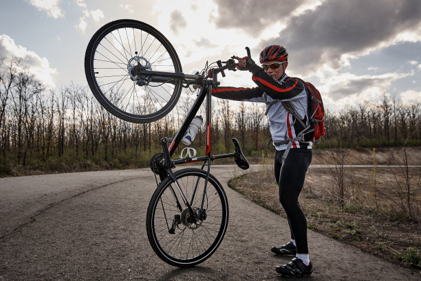 一个运动员骑着自行车在马路上，背景是天空，太阳在云里。图片下载