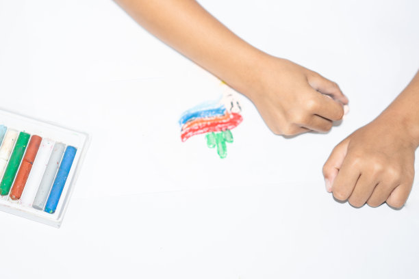 盒子里的蜡笔和手持蜡笔在白色背景的白纸上作画图片下载