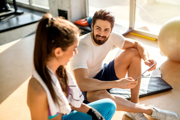 性感强壮的个人健身教练和他的客户坐在健身房聊天的图片。图片下载